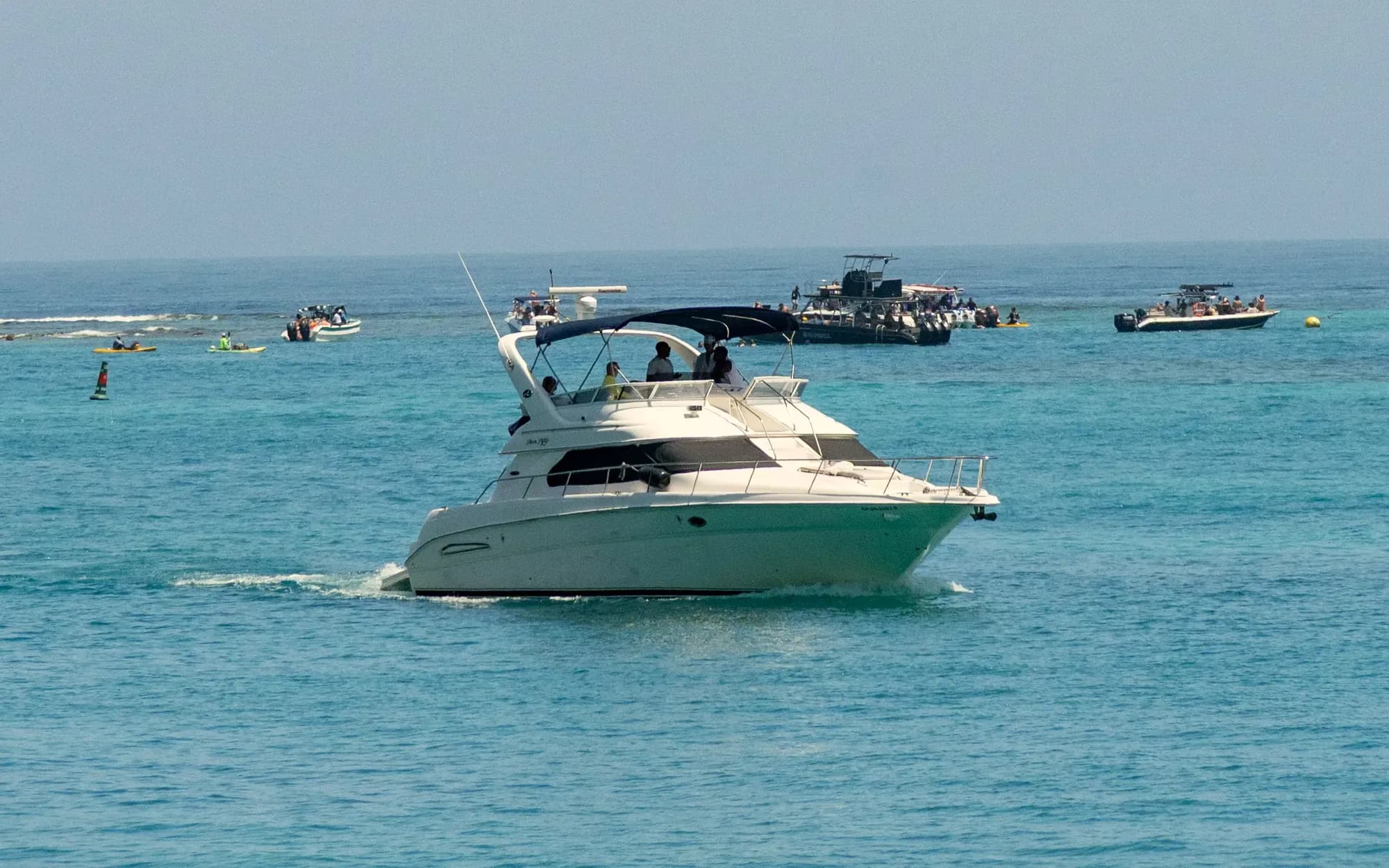 Yate navegando por aguas turquesa en las Islas del Rosario, con botes y kayaks al fondo